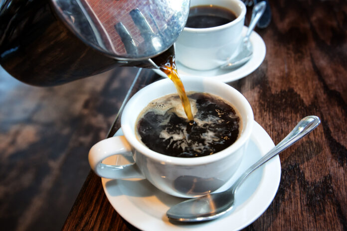 Heißer schwarzer Kaffee wird aus einer French Press in eine weiße Tasse eingegossen.