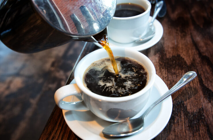 Heißer schwarzer Kaffee wird aus einer French Press in eine weiße Tasse eingegossen.