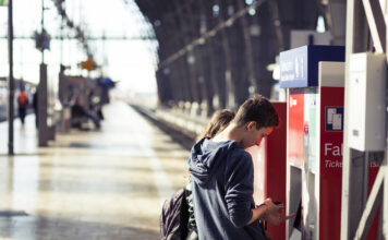 Eine Frau und ein junger Mann kaufen an einem Ticket-Automaten am Gleis an einem Deutschen Bahnhof ein Ticket für einen Regionalzug oder einen ICE.