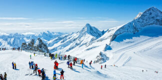 Viele Erwachsene und Kinder auf einer Skipiste in den Bergen beim Skilaufen