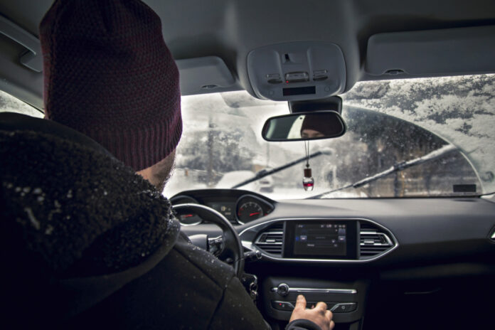 Ein Mann fährt mit einer Mütze im Auto. Draußen liegt Schnee.