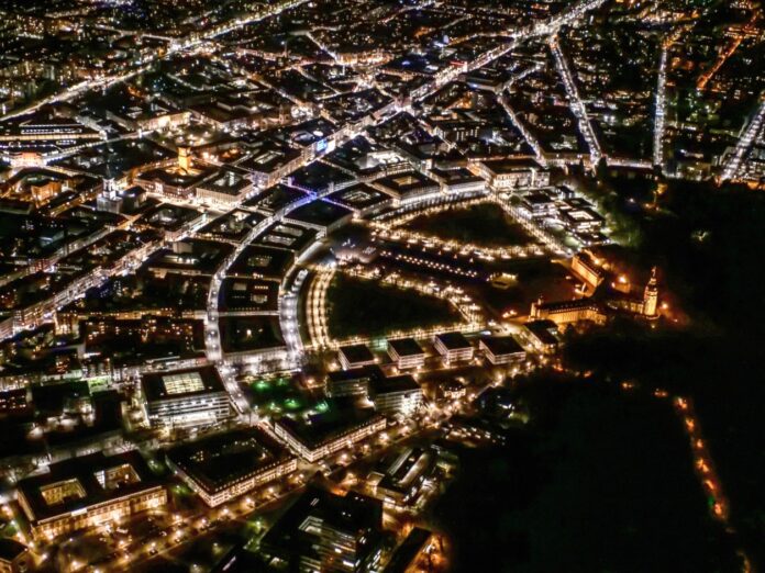 Ein Luftbild von Karlsruhe bei Nacht, die Fächerstadt mit Straßenbeleuchtung. Die Lichter sind angeschaltet in den Wohnungen und Häusern, in denen die Bürger der Fächerstadt leben.