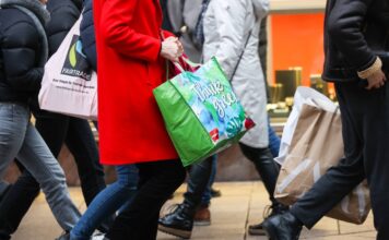 Mehrere Kunden mit Geschenktüten laufen durch eine Innenstadt, sie waren einkaufen