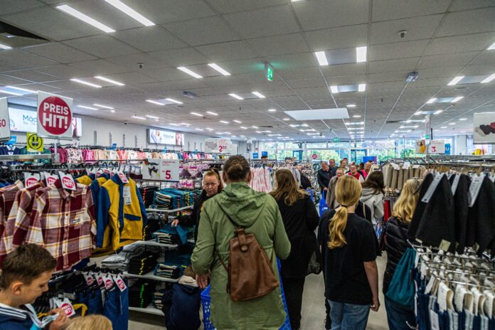 Der Schlussverkauf in einem Geschäft für Kleidung mit vielen Kunden. Die Besucher bummeln durch den Laden und schauen nach Produkten, Anziehsachen und Rabatten.