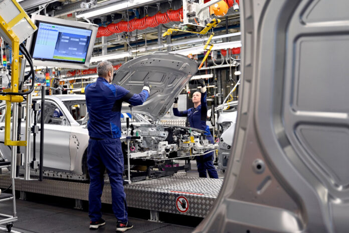 Ein Arbeiter steht an einem Fließband in einer Fabrik, in der Autos produziert werden.