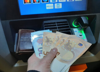 Ein Mann hebt Geld am Geldautomaten ab. In der Hand hält er verschiedene 50- und 20-Euro-Scheine, die er zu einem Fächer aufgereiht hat.