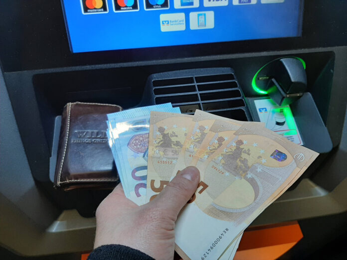 Mann hebt Geld am Geldautomat ab.