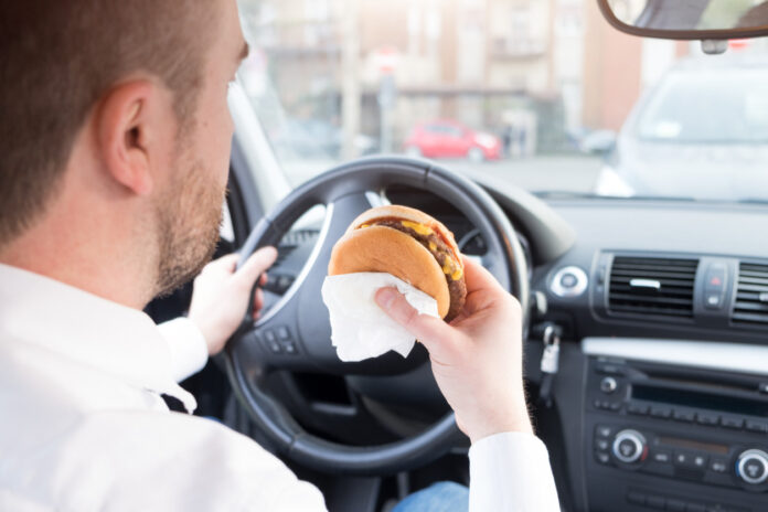 Ein Mann isst einen Burger im Auto.