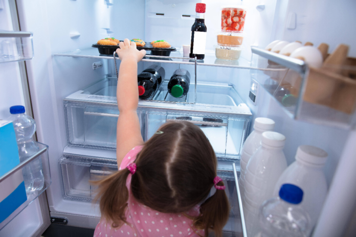 Ein Mädchen greift Lebensmittel im Kühlschrank