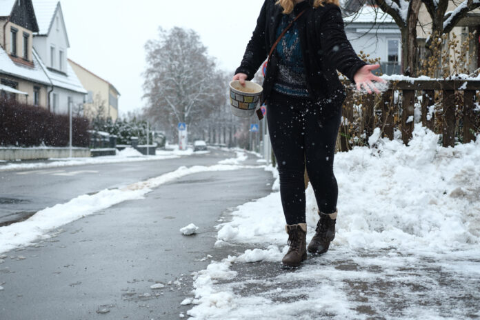 Eine Frau streut Salz bei Schnee auf die Straße