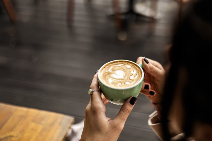 Eine unkenntliche Frau hält eine Tasse Kaffee mit Milch in der Hand