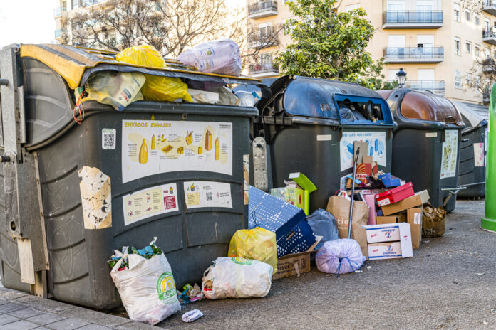 Überfüllte Mülltonnen in der Innenstadt mit Säcken und Müllbeuteln an der Seite.