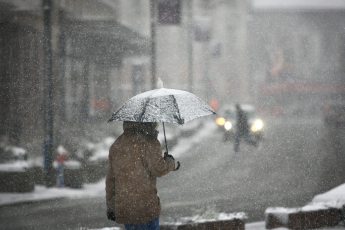 EIn Mann läuft mit einem Regenschirm durch eine verschneite Straße.