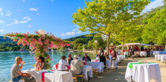 Gäste sitzen auf einer Terrasse eines Restaurants direkt neben dem Wasser eines Sees oder eines Flusses