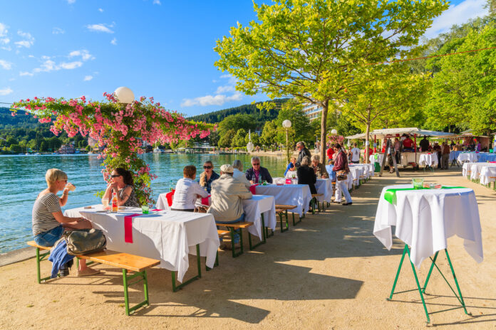 Gäste sitzen auf einer Terrasse eines Restaurants direkt neben dem Wasser eines Sees oder eines Flusses