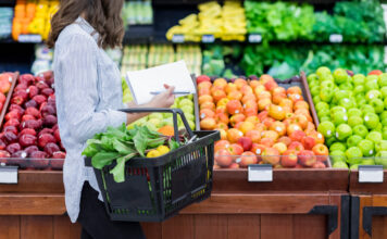 Eine Frau im Supermarkt mit einem Korb Obst und Gemüse.