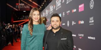 Sally steht neben ihrem Mann Murat Özcan bei einem öffentlichen Event auf dem roten Teppich vor einer Werbetafel vor der Kamera