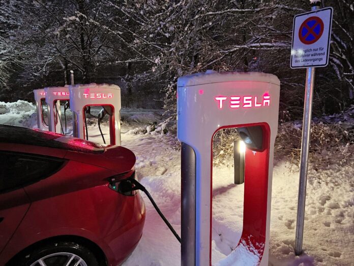 Ein Tesla Elektroauto lädt an einer Tesla Ladesäule im Schnee.