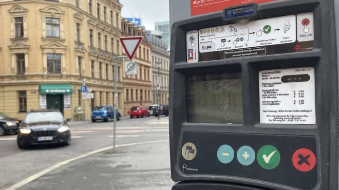 An einer Straße steht ein Parkautomat, aus dem Autofahrer ein Ticket ziehen können. Viele teilen sich ein Ticket.