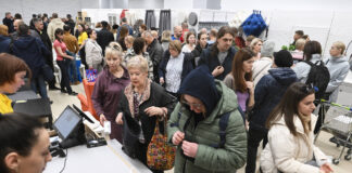 Viele verschiedene Menschen stehen an der Kasse bei Ikea, um ihre ausgesuchten Produkte bei den Mitarbeitern der Möbelkette zu bezahlen. Sie halten Taschen und Geldbörsen in der Hand während sie in der Warteschlange stehen
