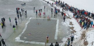 Menschen baden im Winter an einem Badesee und stehen versammelt an einer Eisfläche. Hunderte stellten einen neuen Rekord auf.