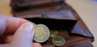 Eine Hand hält eine 2-Euro-Münze, die eine Person aus dem Portemonnaie genommen hat. Weitere Münzen befinden sich im Geldbeutel.