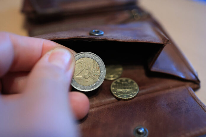 Eine Hand hält eine 2-Euro-Münze, die eine Person aus dem Portemonnaie genommen hat.