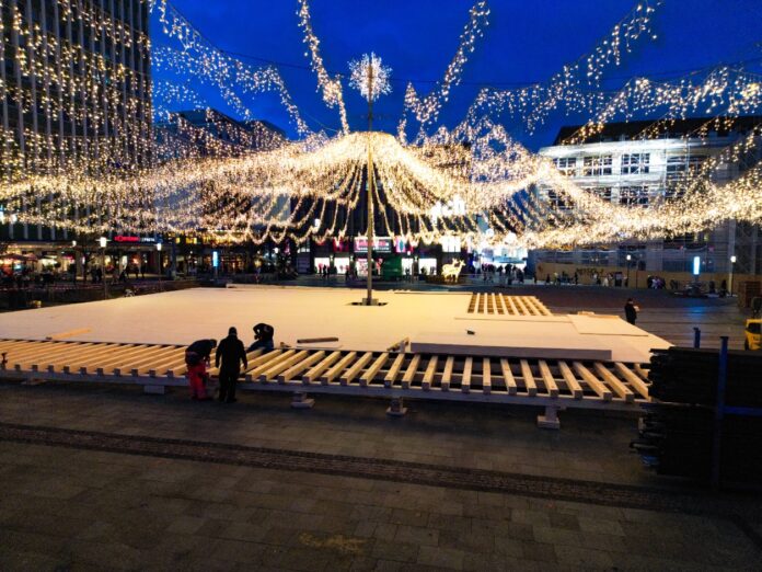 Mitarbeiter bauen eine Bühne und installieren Lichter in einer Innenstadt am Abend für eine Veranstaltung