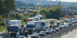 Autos und LKW stehen auf der Autobahn im Stau. Es ist viel Verkehr und die Fahrzeuge stehen auf der Straße eng beieinander.