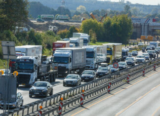Autos und LKW stehen auf der Autobahn im Stau. Es ist viel Verkehr und die Fahrzeuge stehen auf der Straße eng beieinander.