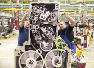 Zwei Männer in blauer Arbeitskleidung arbeiten an der Montage einer Maschine in dem Werk eines Unternehmens in Baden-Württemberg. Zu sehen sind verschiedene Teile der Maschine.