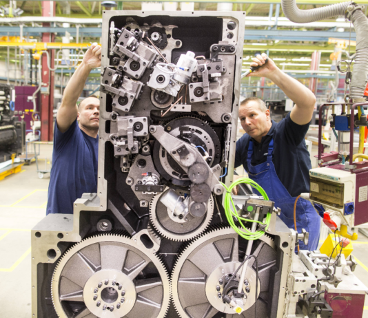 Zwei Männer in blauer Arbeitskleidung arbeiten an der Montage einer Maschine in dem Werk eines Unternehmens in Baden-Württemberg. Zu sehen sind verschiedene Teile der Maschine.