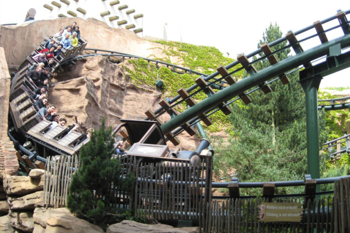 Eine Achterbahn im Phantasialand führt in einen Felsen hinein. Davor ist der Wartebereich abgebildet, welcher auf dem Bild menschenleer ist.