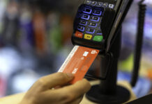 Eine Frau bezahlt mit ihrer EC-Karte der Sparkasse an einem EC-Karten-Lesegerät. Die Karte sowie das Gerät stehen klar im Fokus, der Hintergrund ist unerkennbar verschwommen.