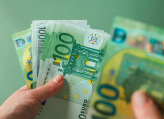 Eine weibliche Hand hält mehrere Hundert-Euro-Scheine. Sie blättert durch die Banknoten und zählt sie. Die Scheine leuchten grün und es sind sowohl alte, als auch neue Geldscheine dabei.