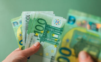 Eine weibliche Hand hält mehrere Hundert-Euro-Scheine. Sie blättert durch die Banknoten und zählt sie. Die Scheine leuchten grün und es sind sowohl alte, als auch neue Geldscheine dabei.