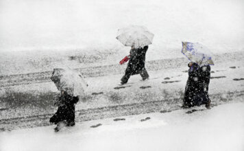 Menschen mit Schirmen gehen im Schnee.