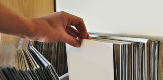 Eine Hand durchsucht die Schallplatten in einem Regal.