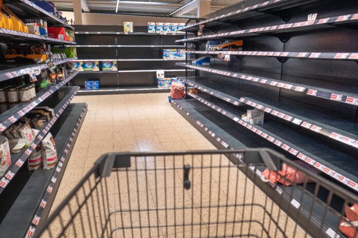 Ein Einkaufswagen fährt durch einen Supermarkt mit leeren Regalen.