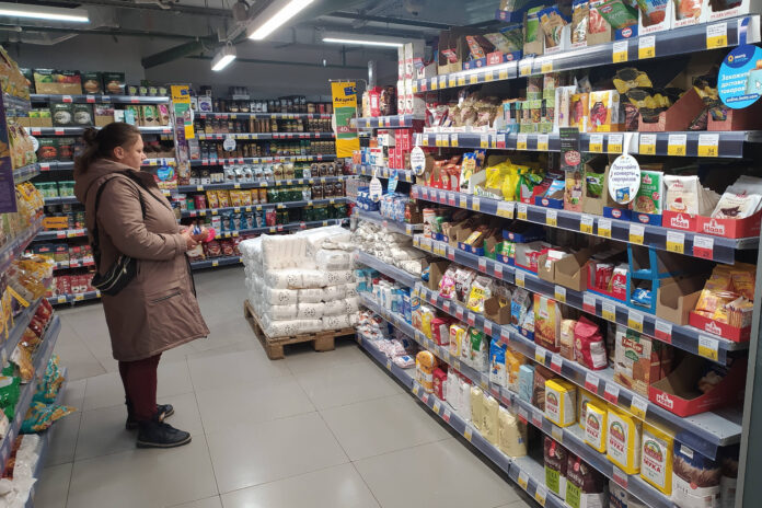 Eine Frau steht in einem Supermarkt vor einem Regal und sieht sich die Lebensmittel an. Ein weiteres Grundnahrungsmittel wird teurer.