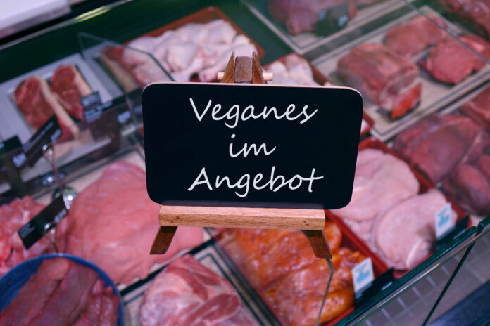 Eine Fleischtheke in einer Metzgerei mit einem Schild, das Veganes anbietet.