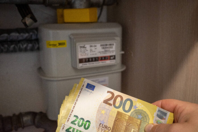 Vor einem Stromzähler hält eine Hand mehrere 200 Euro Scheine