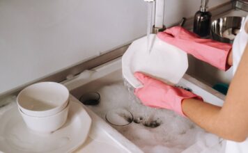 Eine Frau mit pinken Gummihandschuhen wäscht Geschirr im Spülbecken.