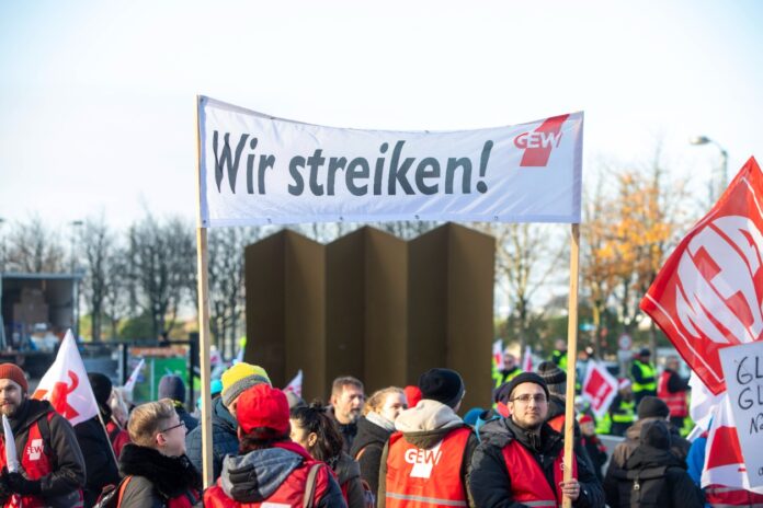 Mehrere Streikende nehmen an einem Protest Teil der Gewerkschaft und zeigen ein Banner mit der Aufschrift: wir streiken. Nun legen Großbetriebe in Karlsruhe ihre Arbeit nieder.