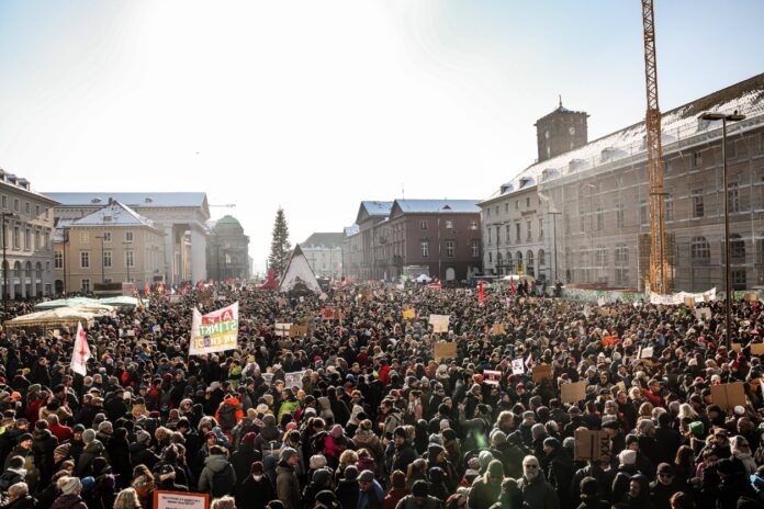 Zahlreiche Menschen kommen auf einer Demonstration in Karlsruhe in der Innenstadt zusammen. Die Menschenmasse versammelt sich, darunter sind Erwachsene und Kinder. Im Hintergrund sind die Häuser der Stadt und die Straßen zu sehen.
