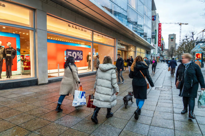 Menschen in einer Einkaufsstraße laufen vor einem Bekleidungsgeschäft vorbei. Harte Peek & Cloppenburg Insolvenz-Maßnahme trifft nun alle Filialen.