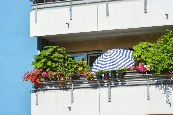 Ein Balkon eines Hochhauses ist mit Pflanzen und einem Sonnenschirm ausgestattet.