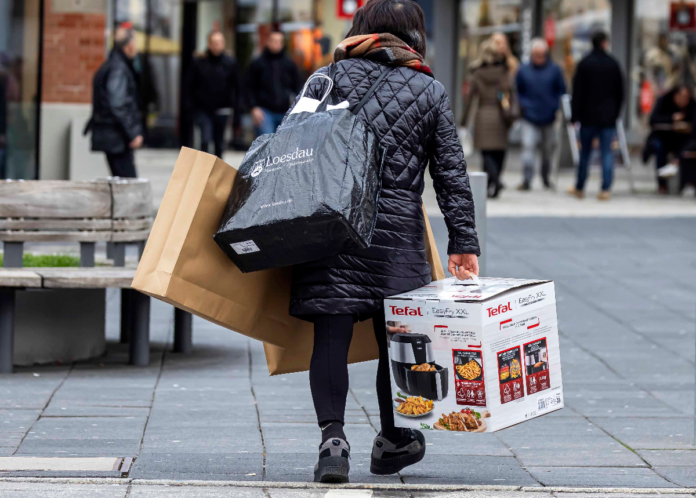 Eine Frau von hinten in schwarzer Kleidung. Sie ist voll gepackt mit Einkaufstüten und Taschen, sie kommt vom Shoppen und läuft durch die Fußgängerzone der Innenstadt.