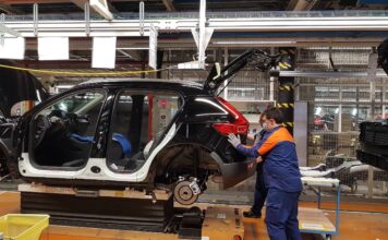 Ein Auto ohne Türen wird in einer Halle einer Fabrik von einem Mitarbeiter mit den Händen am Kofferraum in der Produktion zusammengebaut.