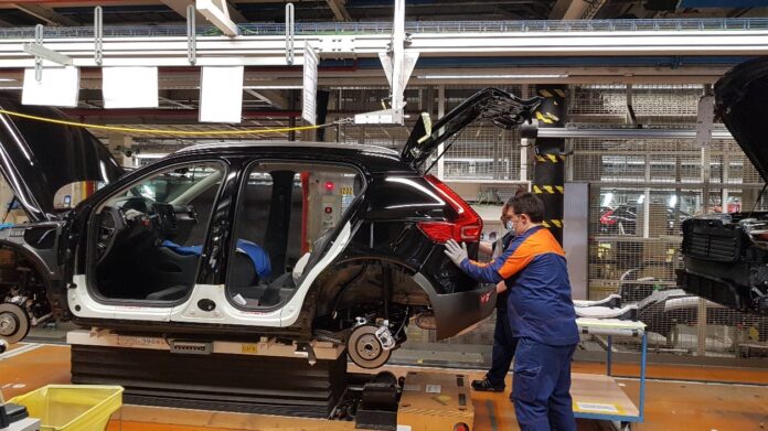 Ein Auto ohne Türen wird von einem Mitarbeiter in der Produktion zusammengebaut.